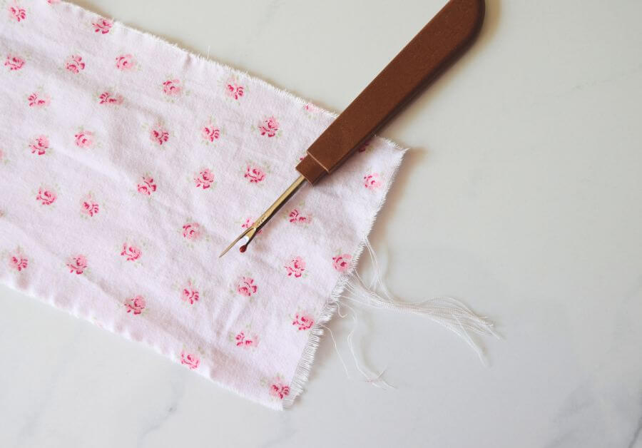a seam ripper on top of a piece of pink floral material with frayed edges