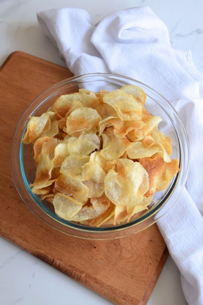 homemade kettle chips in a glass bowl on a wooden cutting board