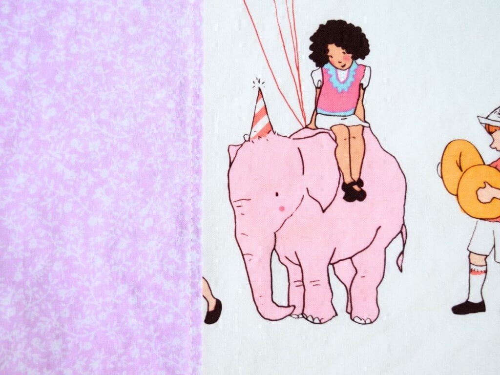 a piece of purple floral fabric top stitched to another piece of fabric with an elephant and a girl on it